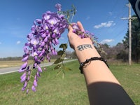 a hand holding a purple flower with a tattoo on it